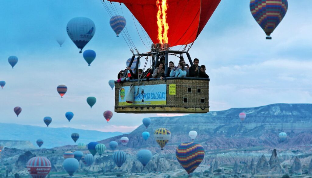 People enjoying a ride in a hot air balloon floating over the unique rock formations and scenic landscapes of Cappadocia during sunrise.