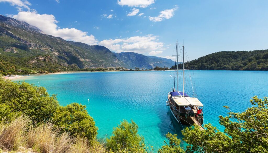 A scenic aerial view of the Turquoise Coast in Turkey, featuring crystal-clear blue waters, lush green hills, and rocky shorelines.